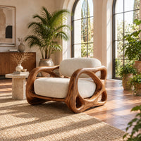 Armchair with looping carved wood arms and plush cream cushions in a bright living room with arched windows and plants