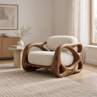 Armchair with looping carved wood arms and plush cream cushions in a Scandinavian living room with white walls