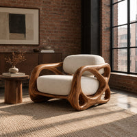 Armchair with looping carved wood arms and plush cream cushions in an industrial loft living room with exposed brick