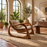 Lounge chair with looping wooden arms and an open oval base in a bright living room with arched windows and plants