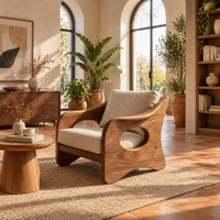 Lounge chair with oval side cutouts and tan cushions in a bright living room with arched windows and plants