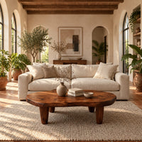 Low bean shaped coffee table with a rich grained top and four tapered legs in a bright living room with arched windows and plants