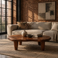 Low bean shaped coffee table with a rich grained top and four tapered legs in an industrial loft living room with exposed brick