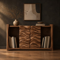 Low bookshelf with two carved wave doors and open bays at both ends in a dark studio against a charcoal plaster wall