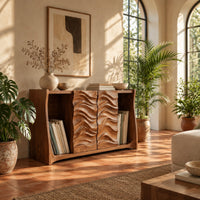 Low bookshelf with two carved wave doors and open bays at both ends in a bright living room with arched windows and plants
