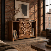 Low bookshelf with two carved wave doors and open bays at both ends in an industrial loft living room with exposed brick