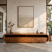 Corner detail of low capsule shaped tv stand with wave carved fronts and open bays beside wood, brass and linen samples