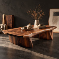 Corner detail of low coffee table with a thick slab top and two boat shaped legs beside wood, brass and linen samples