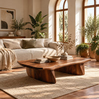 Low coffee table with a thick slab top and two boat shaped legs in a bright living room with arched windows and plants