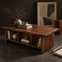 Corner detail of low coffee table with a wavy natural edge top and three open cubbies beside wood, brass and linen samples