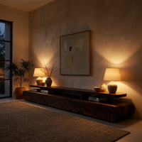 Low drawer plinth TV stand with a floating shelf in an evening room lit by two lamps