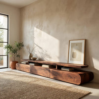 Low drawer plinth TV stand with a floating shelf in a sunlit room with large windows and plants