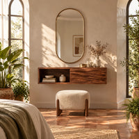 Floating makeup vanity with an open cubby and a wave carved front panel in a bright bedroom with arched windows and plants