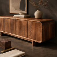 Corner detail of low wood sideboard with four flat front panels and short legs beside wood, brass and linen samples