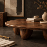 Corner detail of low oval coffee table with a thick top and chunky pod shaped legs beside wood, brass and linen samples