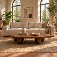 Low oval coffee table with a thick top and chunky pod shaped legs in a bright living room with arched windows and plants