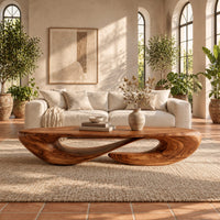 Low oval coffee table on a twisted open loop base in a bright living room with arched windows and plants