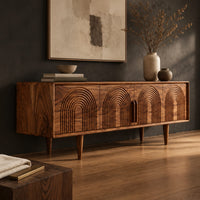 Corner detail of long sideboard with four doors carved with nested arches on tapered legs beside wood, brass and linen samples
