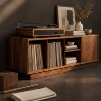 Corner detail of low wood record console with three open cubbies and a panel end beside wood, brass and linen samples