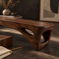Corner detail of low slab top bench with open triangular legs beside wood, brass and linen samples