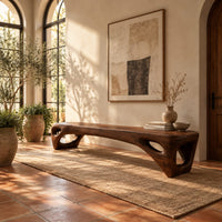 Low slab top bench with open triangular legs in a bright entryway with arched windows and plants