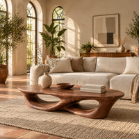 Low coffee table with an oval top and twin open loops in a bright living room with arched windows and plants