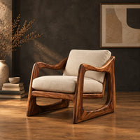 Low lounge chair with looped side frames, sloped arms and cream cushions in a dark studio against a charcoal plaster wall