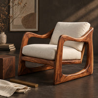 Corner detail of low lounge chair with looped side frames, sloped arms and cream cushions beside wood, brass and linen samples
