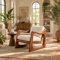 Low lounge chair with looped side frames, sloped arms and cream cushions in a bright living room with arched windows and plants