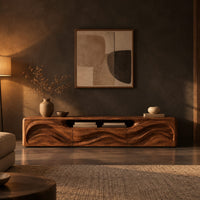 Low wood tv stand with a rippling carved front and an open top slot in a dark living room at golden hour