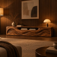 Low wood tv stand with a rippling carved front and an open top slot in an evening living room with walnut wall paneling