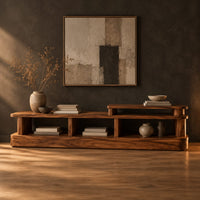 Low stepped open shelf console table with a raised section at one end in a dark studio against a charcoal plaster wall