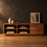 Low storage bench with four open cubbies and a closed wood panel in a dark studio against a charcoal plaster wall