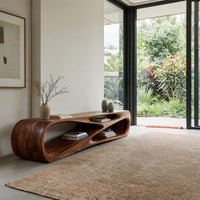 Low TV console with a carved crossing hollow in a sunlit room with large windows and plants