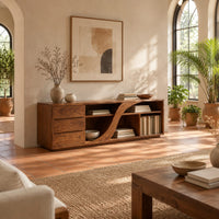 Low tv stand with three drawers and a swooping divider beside vertical slots in a bright living room with arched windows and plants