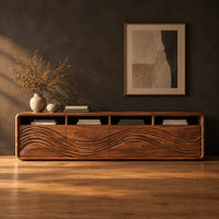 Low tv stand with four open cubbies above wave carved front panels in a dark studio against a charcoal plaster wall