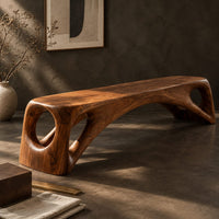 Corner detail of low solid wood bench with an arched underside and open cutouts at each end beside wood, brass and linen samples