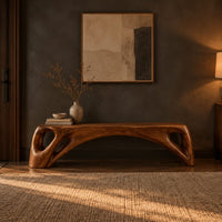 Low solid wood bench with an arched underside and open cutouts at each end in a dark entryway at golden hour