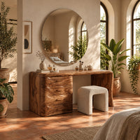 Makeup vanity desk with four wave carved drawers and a single slab leg in a bright bedroom with arched windows and plants