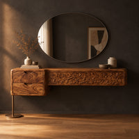 Makeup vanity with a carved vine panel, two drawers and a slim post leg in a dark studio against a charcoal plaster wall