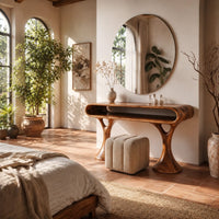 Makeup vanity with a pill shaped open shelf top and flared pedestal legs in a bright bedroom with arched windows and plants