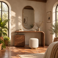 Makeup vanity with a waterfall end and a three drawer cabinet in a bright bedroom with arched windows and plants