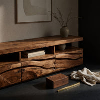 Corner detail of media cabinet with open cubbies above carved wave drawers beside wood, brass and linen samples