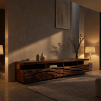 Media cabinet with open cubbies above carved wave drawers in an evening room lit by two lamps