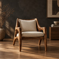 Wooden armchair with sweeping sculpted arms and splayed legs in a dark studio against a charcoal plaster wall