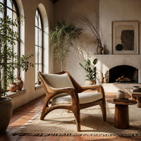 Wooden armchair with sweeping sculpted arms and splayed legs in a bright living room with arched windows and plants