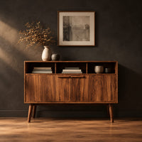 Mid century console table with three open cubbies and two doors on tapered legs in a dark studio against a charcoal plaster wall