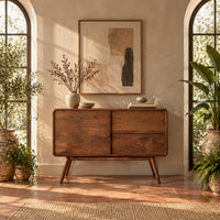 Low cabinet style console table with three wood panels on splayed legs in a bright entryway with arched windows and plants