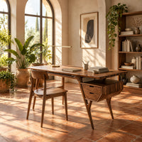 Mid century desk with tapered legs and a wedge shaped two drawer box in a bright home office with arched windows and plants