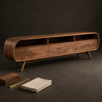 Corner detail of low tv stand with pill shaped ends, three open cubbies and slim tapered legs beside wood, brass and linen samples